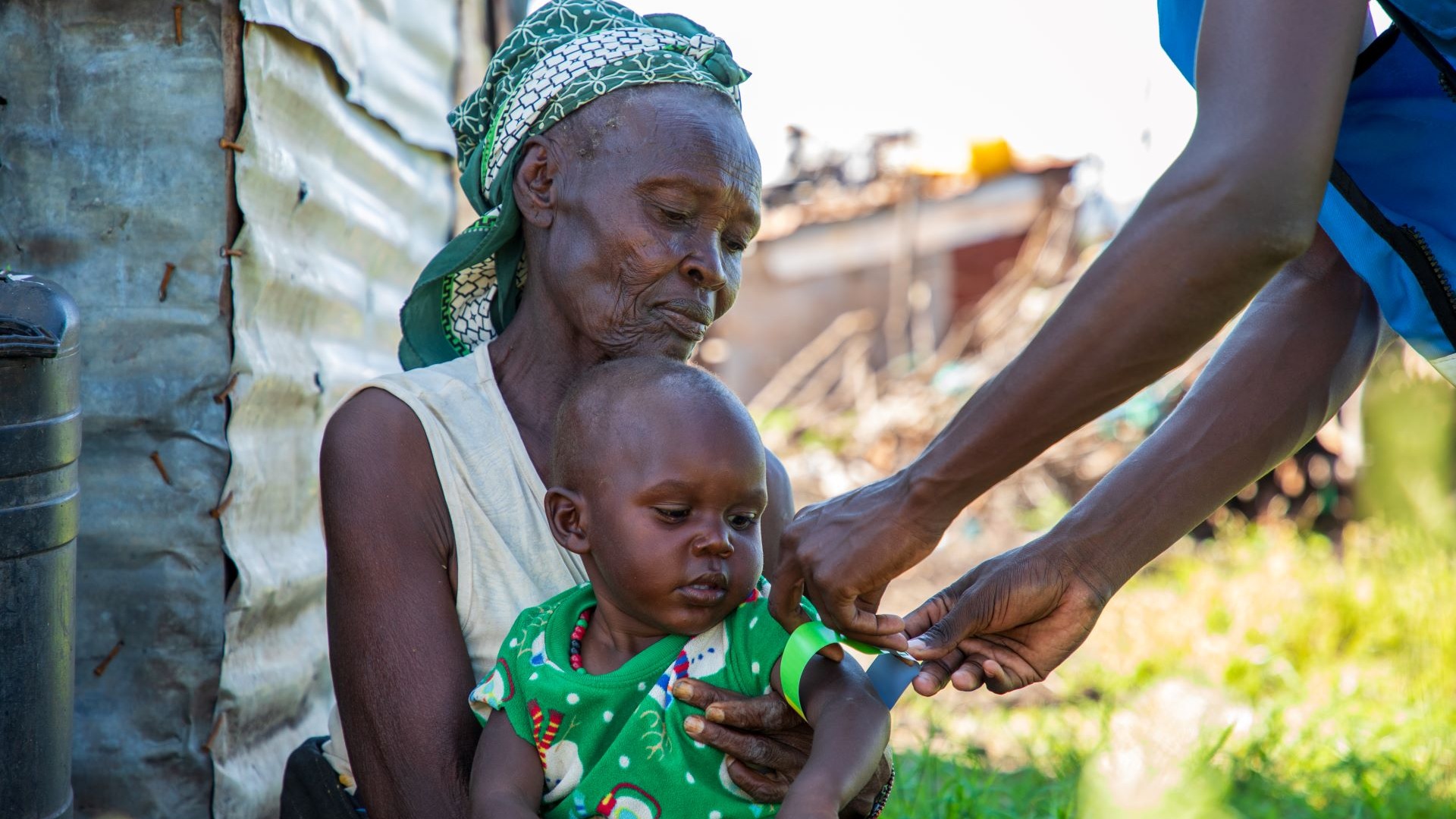 Mother holding a child while an aid worker measures the child's malnutrition level