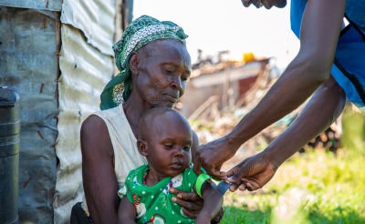 Mother holding a child while an aid worker measures the child's malnutrition level