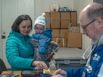 A woman holding her child next to an Action Against Hunger social worker in Ukraine.