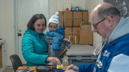 A woman holding her child next to an Action Against Hunger social worker in Ukraine.