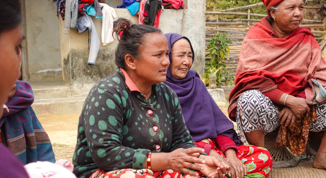 A Nepali woman sitting cross-legged on the floor with other women in a circle.