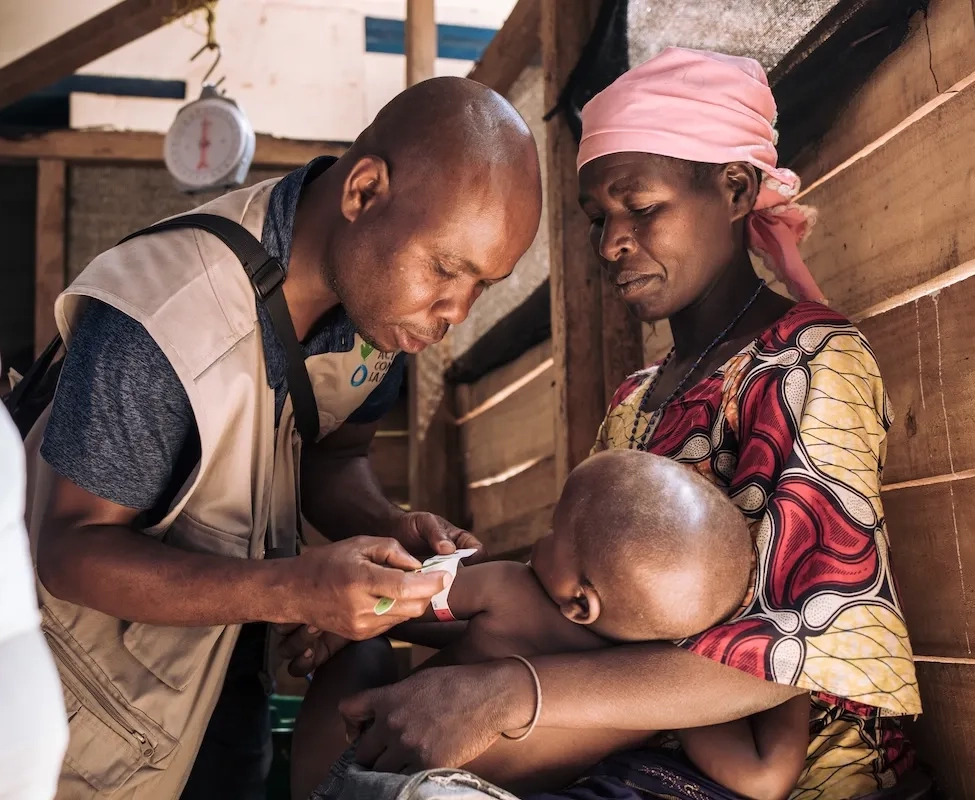 A health worker checks the nutrition status of a young boy as his mother holds him.